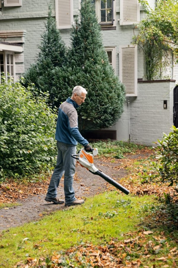 Un homme soufflant les feuilles de son jardin
